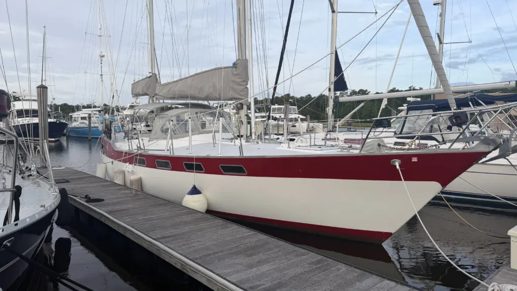 A red-hulled sailboat lying alongside a dock