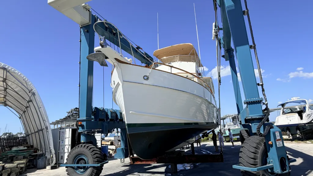 A motor yacht lifted in a Travelift sling at a boatyard, hauled out for a pre-purchase survey